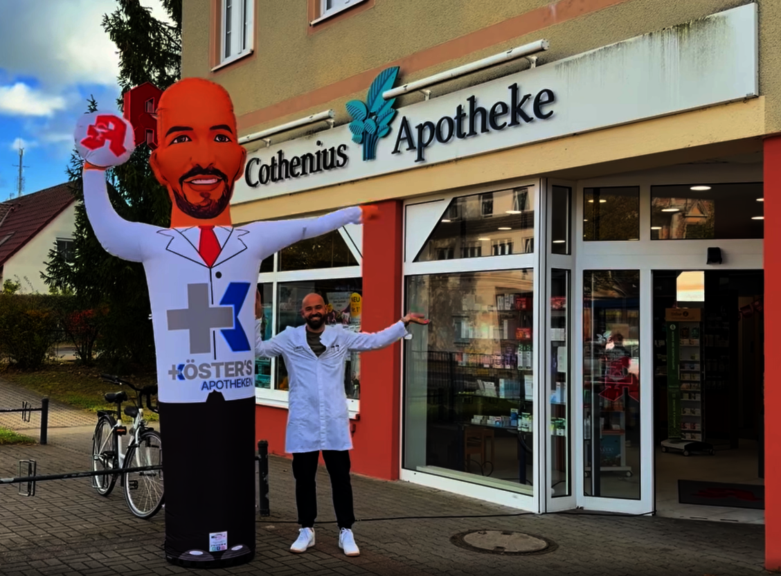 Apothekeninhaber Florian Köster mit seinem Winkemännchen vor seiner Apotheke. / © Florian Köster/ Cothenius-Apotheke
