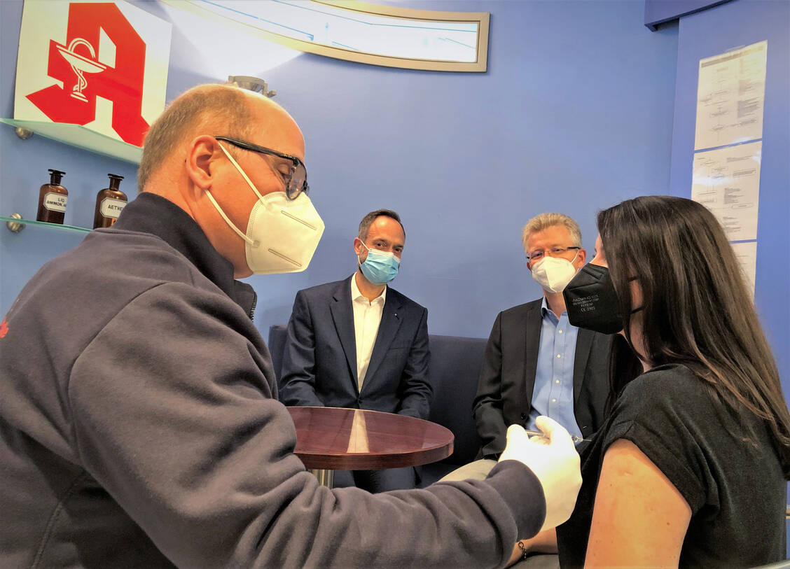 Apotheker Michael Beckmann impft Patientin Irina Schessler. Im Hintergrund: Thomas Rochell (rechts), Vorstandsvorsitzender des Apothekerverbandes Westfalen-Lippe, und Tom Ackermann, Vorstandsvorsitzender der AOK Nordwest. / Foto: AVWL/Grunsky