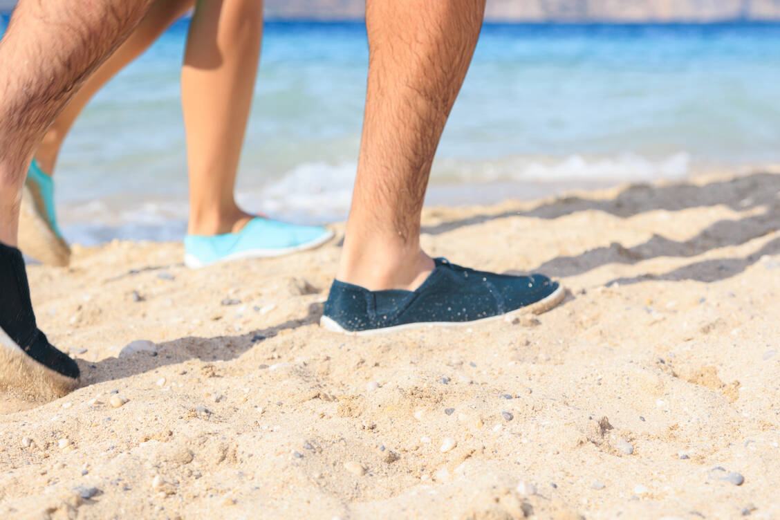 Wer sich vor kutaner Larva migrans schützen will, dem empfehlen Experten das Tragen von Schuhen am Strand. Die Infektion erfolgt typischerweise beim Barfußlaufen auf Sand, der mit dem Kot infizierter Tiere verunreinigt ist. / © Getty Images/Liubov Isaeva