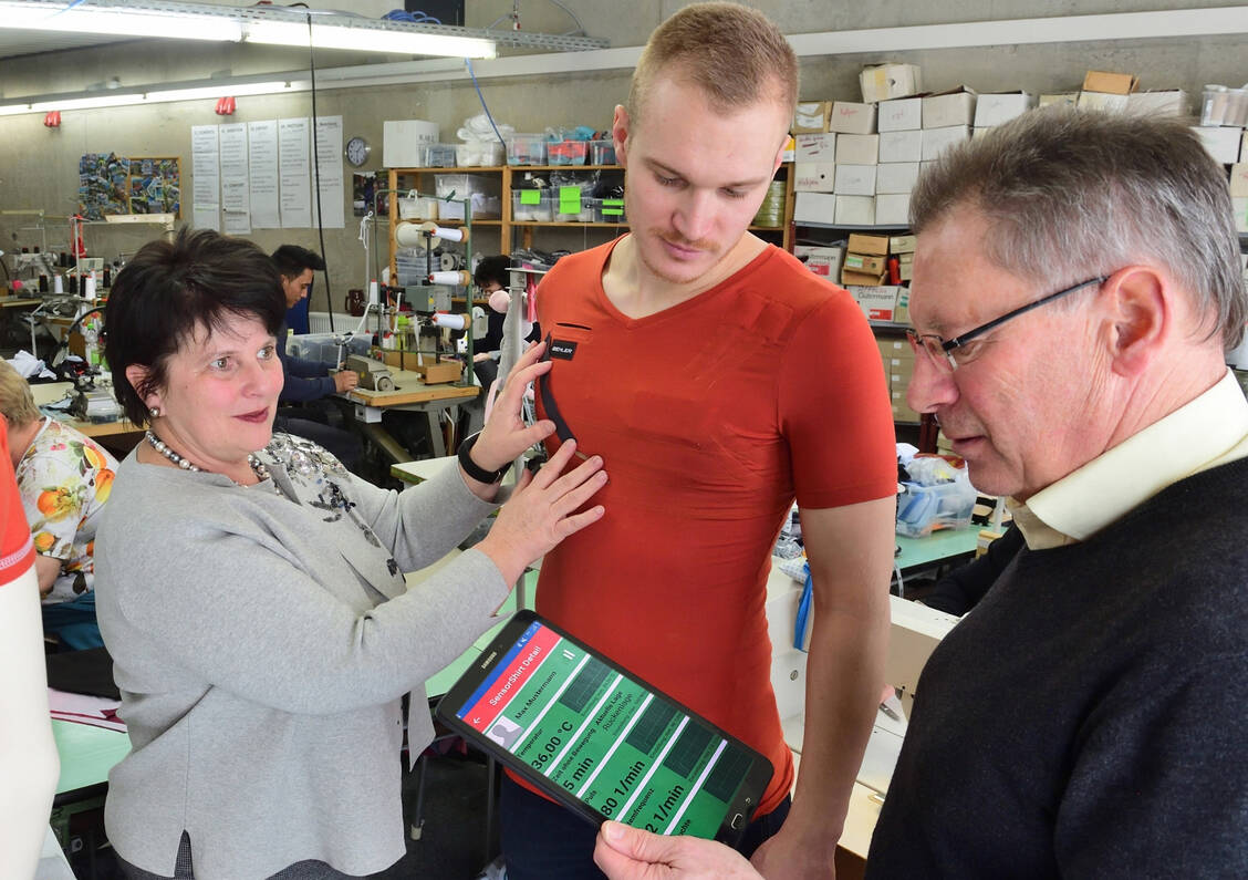 Biehler-Chefin Steffi Barth testet mit Mitarbeiter Philipp Zwingenberger und Reinhard Helbig vom Sächsischen Textilforschungsinstitut (STFI) ein Funktionsmuster des neuen Sensor-Pflegeshirts sowie die dazugehörige App. / Foto: Wolfgang Schmitd
