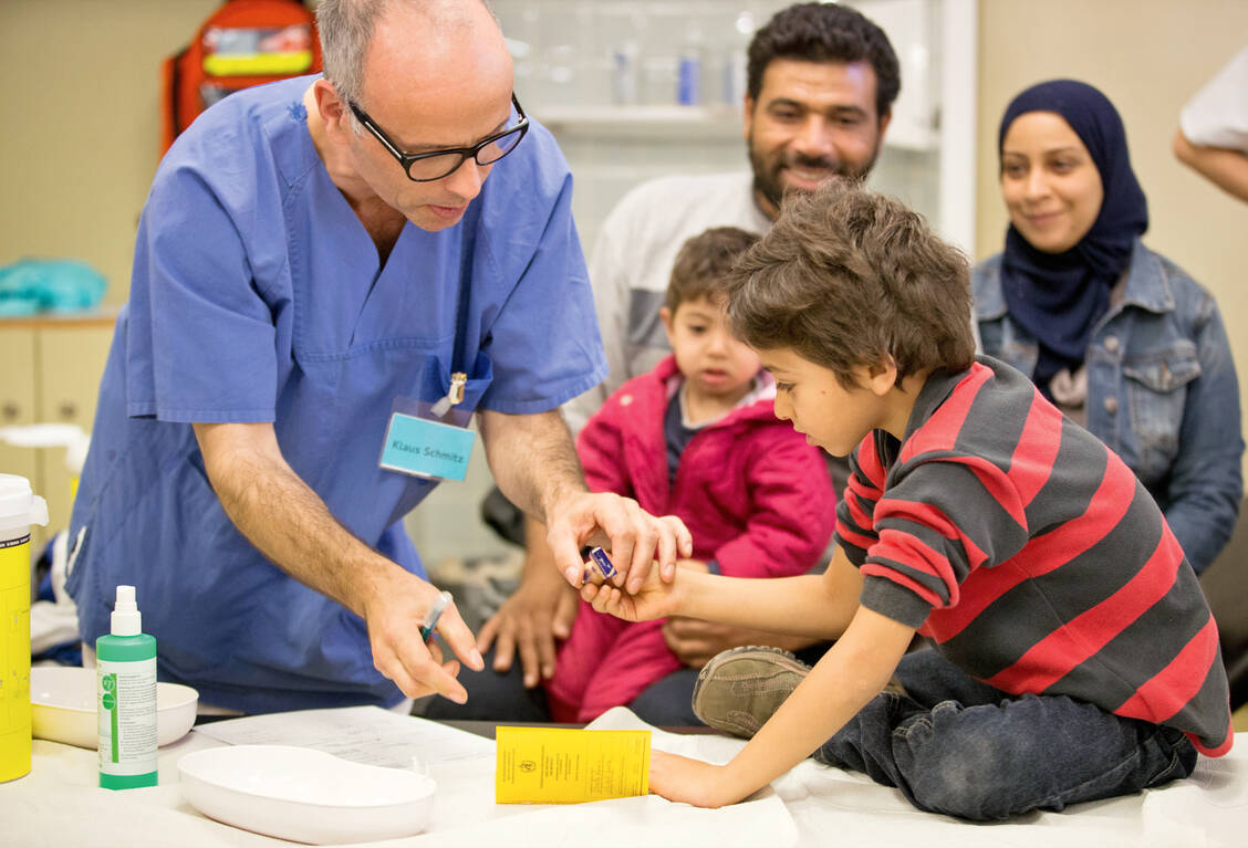 Ein syrischer Flüchtlingsjunge stempelt am 1. Oktober 2015 in Berlin im Landesamt für Gesundheit und Soziales seinen neuen Impfausweis. In einigen Ländern können aufgrund von Kriegen und mangelnder Infrastruktur viele Kinder nicht geimpft werden. / Foto: dpa/Kay Nietfeld