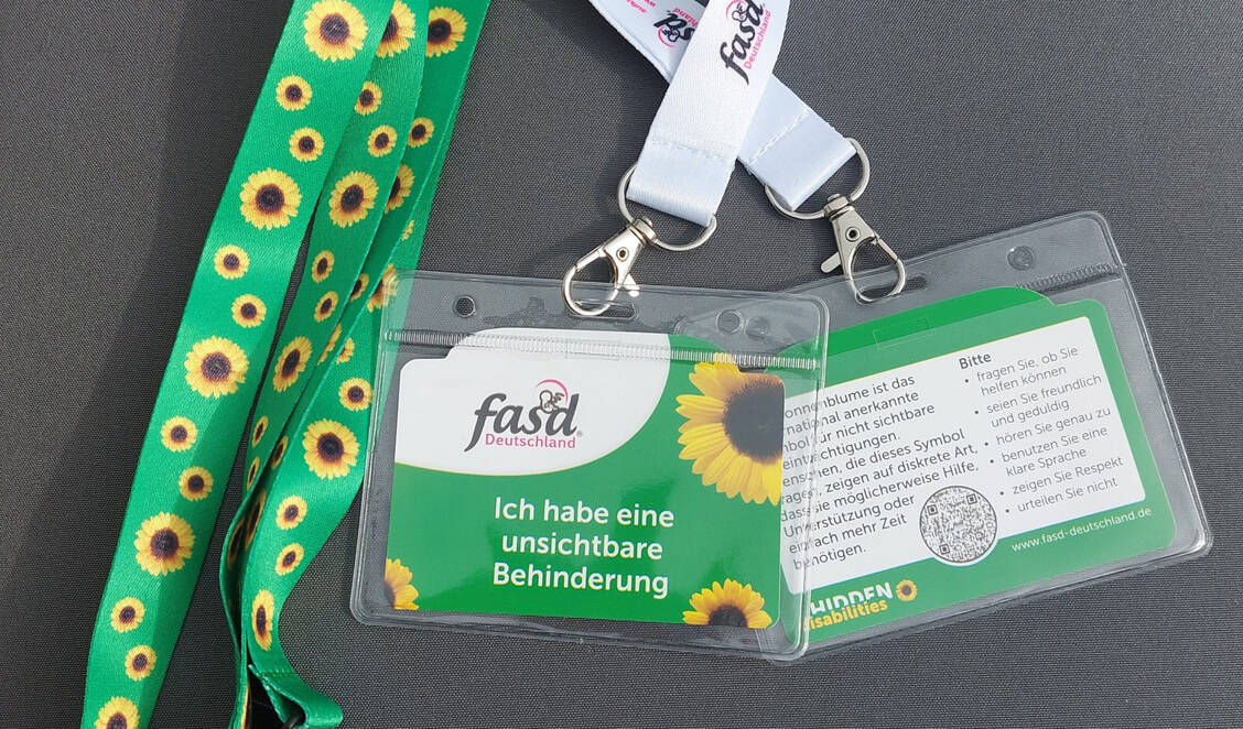 Umhängebänder mit Sonnenblume sind ein international anerkanntes Symbol für nicht sichtbare Beeinträchtigungen. Der Verein FASD Deutschland hat dazu eine Textkarte entwickelt, die auf die unsichtbare Behinderung hinweist. / © FASD Deutschland