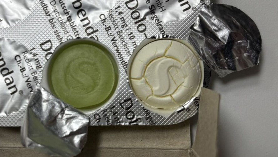 Ein irritierender Anblick: Vermutlich ist die ursprünglich grüne Dolo-Dobendan-Lutschtablette aufgrund einer Rekristallisation des Zuckeraustauschstoffs Isomalt an der Oberfläche weiß verfärbt. Normalerweise sind die Tabletten homogen grün gefärbt mit glatter, rissfreier Oberfläche und Prägung. / © AMK